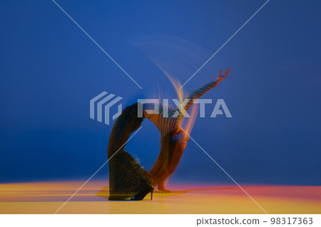 Mixed lights and flexibility. Portrait of young girl dancing heels dance in stylish clothes over blue background in neon light. Concept of modern dance style 98317363
