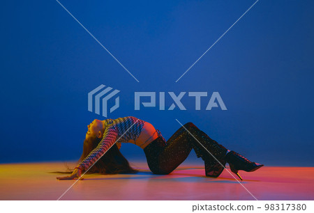 Portrait of young girl dancing heels dance in stylish clothes over blue background in neon light. Concept of modern dance style 98317380