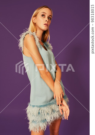 Image of cute beautiful slim blonde woman in elegant cocktail blue dress is posing at studio on purple background. Image of cute beautiful slim blonde woman in elegant cocktail blue dress is posing at studio on purple background. 98318015