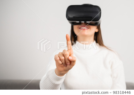 Smiling woman touching air with a finger in VR glasses. Metaverse technology concept.  98318446