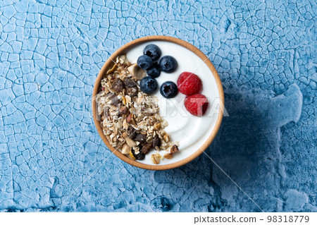 Yogurt with berries and muesli for breakfast in bowl on lbue background Yogurt with berries and muesli for breakfast in bowl on lbue background 98318779