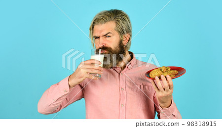 man eating cookies and drinking milk. cookie and a glass of milk. happy farmer eat cookie dessert. bearded man drink useful milk with pastry. Better together for valentines day man eating cookies and drinking milk. cookie and a glass of milk. happy farmer eat cookie dessert. bearded man drink useful milk with pastry. Better together for valentines day 98318915