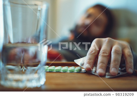 sick man staying in bed taking a pill. closeup view of hand 98319209