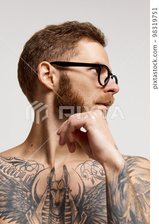 Close up portrait of charming bearded man in eyewear looking at camera confidently over grey background. Concept of emotions, mental health, fashion Close up portrait of charming bearded man in eyewear looking at camera confidently over grey background. Concept of emotions, mental health, fashion 98319751