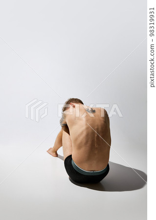 Back view of muscular male fashion model posing isolated over grey studio background. Masculinity. Concept of men's health, beauty, body and skin care, fitness. Body art 98319931