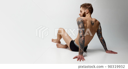 Studio shot of young blonde man with beard and moustache posing shirtless. Perfect muscular body shape. Tattoo body art. Concept of fashion, style, body aesthetics, beauty, men's health 98319932