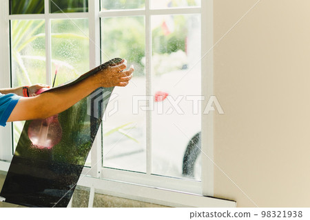 Woker wrapping tinting a house window with tinted foil using foggy spray. 98321938
