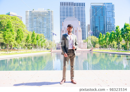 An Indian man wearing a suit standing in a building street and a green park 98323534