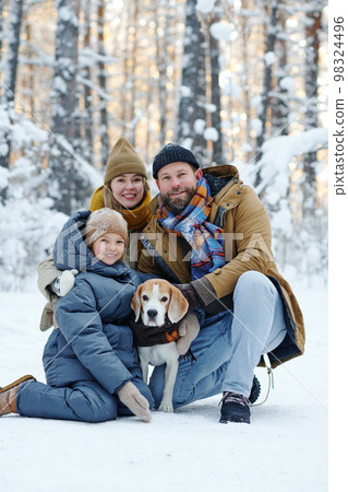 Portrait of happy family smiling at camera while walking with dog in winter forest Portrait of happy family smiling at camera while walking with dog in winter forest 98324496