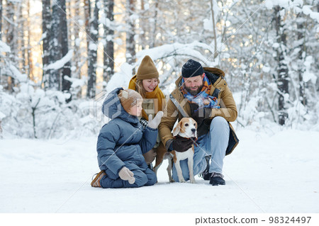 Family of three walking with dog in winter forest during their vacations Family of three walking with dog in winter forest during their vacations 98324497