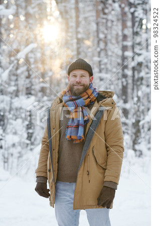 Portrait of young happy man smiling at camera while walking in the forest in winter Portrait of young happy man smiling at camera while walking in the forest in winter 98324522