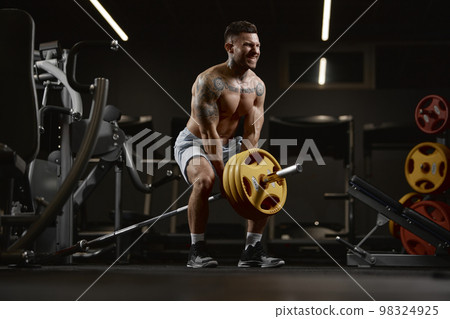 Power. Portrait of young muscular man training shirtless in gym indoors. Lifting barbell exercise. Relief body shape. Concept of sport, workout, strength 98324925