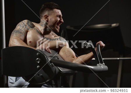 Powerful. Portrait of young muscular man training shirtless in gym indoors. Hand exercises. Workout. Concept of sport, workout, strength Powerful. Portrait of young muscular man training shirtless in gym indoors. Hand exercises. Workout. Concept of sport, workout, strength 98324931