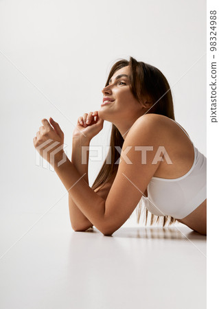 Femininity. Portrait of young beautiful girl with slim fit body posing in white underwear over grey studio background. Concept of body and skin care, fitness 98324988