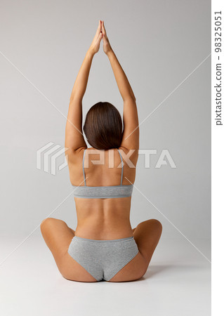 Stretching, yoga. Portrait of young beautiful girl posing in underwear over grey studio background. Rear view. Healthy back. Concept of body and skin care, fitness 98325051