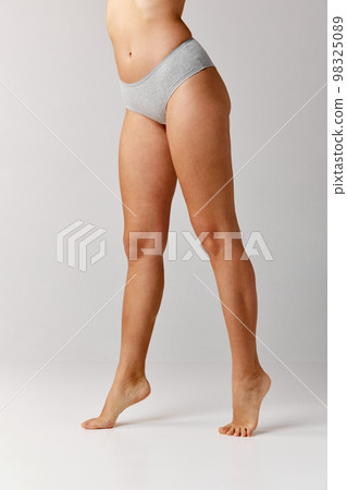 Cropped image of slim, smooth female legs over grey studio background. Model in underwear. Depilation, epilation, laser. Concept of body and skin care, fitness 98325089