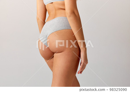 Cropped image of slim, fit female body, buttocks in cotton underwear over grey studio background. Anti-cellulite care. Concept of body and skin care, fitness Cropped image of slim, fit female body, buttocks in cotton underwear over grey studio background. Anti-cellulite care. Concept of body and skin care, fitness 98325090