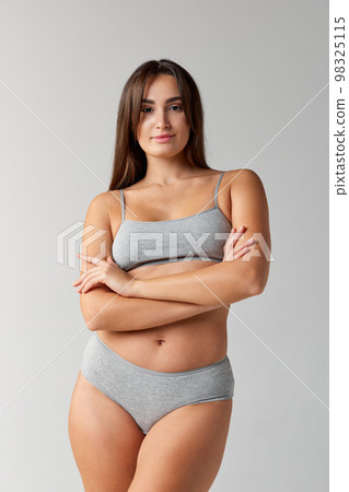 Well-being. Portrait of young beautiful girl posing in underwear over grey studio background. Concept of body and skin care, fitness 98325115