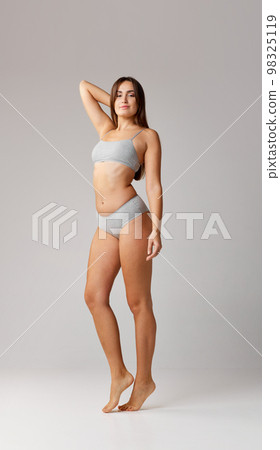 Slim body. Full-length portrait of young beautiful girl posing in cotton underwear over grey studio background. Concept of body and skin care, fitness 98325119