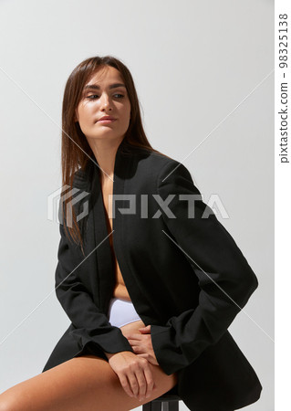 Portrait of young attractive girl posing in black classic suit and underwear over grey studio background. Concept of body and skin care, fitness 98325138