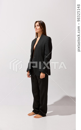 Portrait of young beautiful girl posing black classic suit over grey studio background. Style. Concept of body and skin care, fitness 98325148