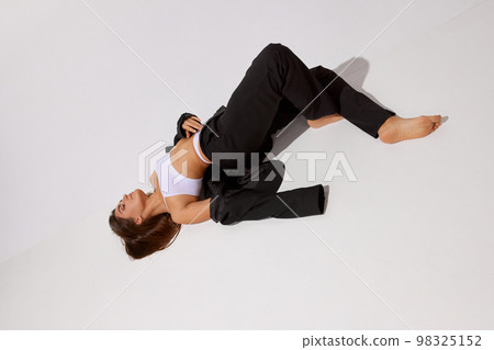 Comfort outfit. Portrait of young beautiful girl posing on floor in underwear and black classic suit over grey studio background. Concept of body and skin care, fitness 98325152