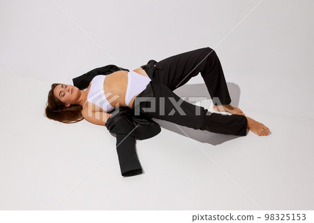 Portrait of young fit girl posing in white underwear and black classic suit over grey studio background. Concept of body and skin care, fitness 98325153