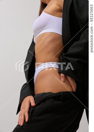 Cropped image of slim female body in white cotton underwear and black classic suit over grey studio background. Concept of body and skin care, fitness Cropped image of slim female body in white cotton underwear and black classic suit over grey studio background. Concept of body and skin care, fitness 98325663