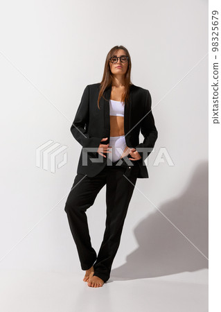 Fashion and comfort. Portrait of young beautiful girl posing in underwear and black classic suit over grey studio background. Concept of body and skin care, fitness 98325679