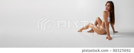 Portrait of young beautiful girl posing on floor in underwear over grey studio background. Banner, flyer. Concept of body and skin care, fitness 98325692