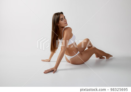 Portrait of young beautiful girl with slim fit body posing in underwear over grey studio background. Concept of body and skin care, fitness 98325695