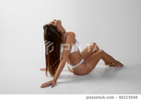 Portrait of young beautiful girl with long brunette hair posing in underwear over grey studio background. Concept of body and skin care, fitness Portrait of young beautiful girl with long brunette hair posing in underwear over grey studio background. Concept of body and skin care, fitness 98325698