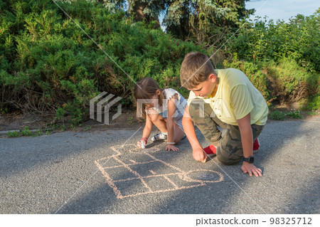 Children draw in chalk on the pavement, in the park at sunset 98325712