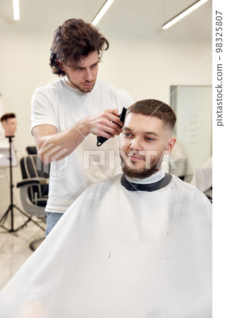 Barber trim hair with clipper on handsome bearded man Barber trim hair with clipper on handsome bearded man 98325807