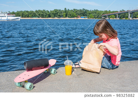 A small child on the promenade with a grocery bag. Sunny summer day, fast food 98325882