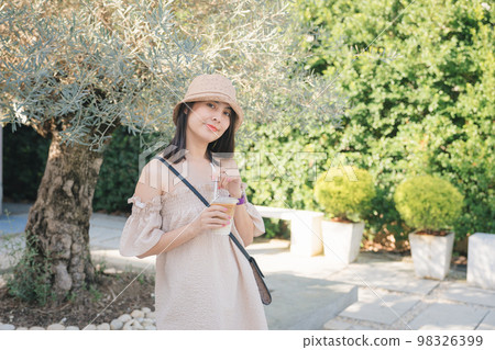 Young asian woman wearing hat and holding iced latte coffee and enjoy in the garden on sunny day 98326399