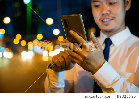 Young man walking and chatting on mobile phone with friends at social networks outdoor, Portrait Asian businessman typing an sms message via smartphone after work near office at night city street 98326589