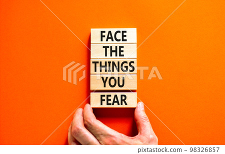 Face the things you fear symbol. Concept words Face the things you fear on wooden blocks on a beautiful orange background. Businessman hand. Business and face the things you fear concept. Copy space. 98326857