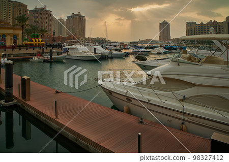 Porto Arabia Marina in The pearl , Doha, Qatar sunset shot showing luxurious yachts and boats docked at the marina with residential buildings in background. Porto Arabia Marina in The pearl , Doha, Qatar sunset shot showing luxurious yachts and boats docked at the marina with residential buildings in background. 98327412