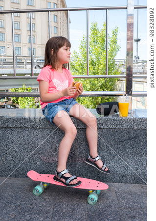 A girl with a sandwich and orange juice is listening to music. Fast food A girl with a sandwich and orange juice is listening to music. Fast food 98328092