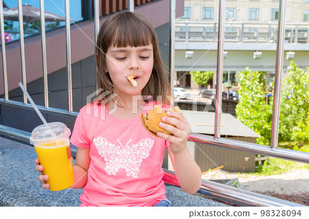 The happy hungry moments of the beautiful girl with a hamburger in to the mouth and by orange juice. Rapid feed. Eating. Unhealthy food, fast fat food The happy hungry moments of the beautiful girl with a hamburger in to the mouth and by orange juice. Rapid feed. Eating. Unhealthy food, fast fat food 98328094