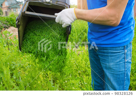 Close-up of a man throwing out freshly cut grass. Cleaning the territory in the open air Close-up of a man throwing out freshly cut grass. Cleaning the territory in the open air 98328126