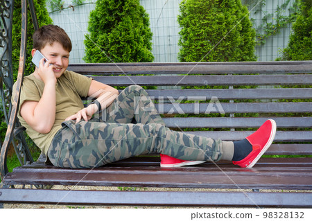 A teenager boy is speaking over the phone in the backyard A teenager boy is speaking over the phone in the backyard 98328132