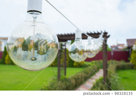 A close-up of an incandescent lamp hanging in the garden backyard A close-up of an incandescent lamp hanging in the garden backyard 98328135