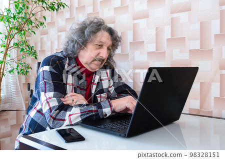 A happy smiling elderly man at the laptop sitting at the table at home 98328151