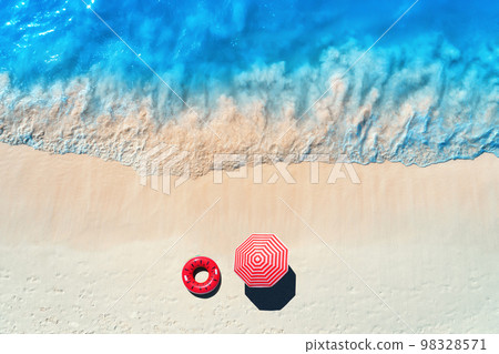 Sandy beach with red swim ring and umbrella at sunset. Top view 98328571