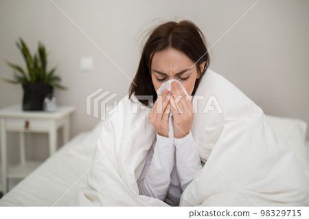 Ill young lady sneezing, staying in bed at home 98329715