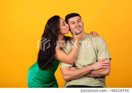 Cheerful millennial arabic female in dress kissing guy on cheek, isolated on orange background, studio Cheerful millennial arabic female in dress kissing guy on cheek, isolated on orange background, studio 98329748