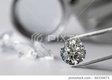 brilliant cut diamond held by tweezers on white background 98330673