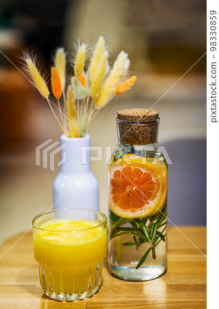 Glass of freshly squeezed juice in glass next to refreshing drink and vase of colorful cereals. Concept of detox Glass of freshly squeezed juice in glass next to refreshing drink and vase of colorful cereals. Concept of detox 98330859